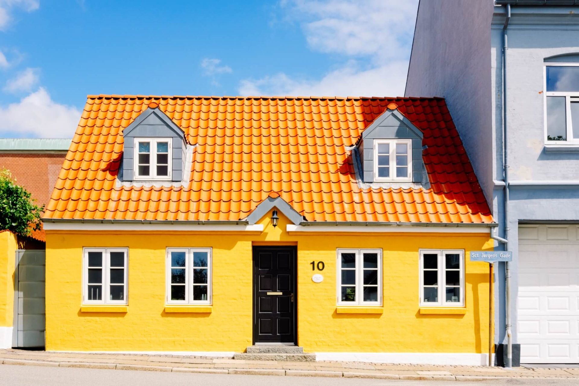 En fastighet i stadsmiljö utmärker sig med sin gula färg, tak i en nyans av orange och dörrar målade i svart